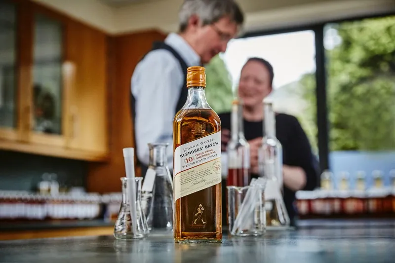 Phhotograph of johnnie walker distillers in background with bottle of Johnnie walker 