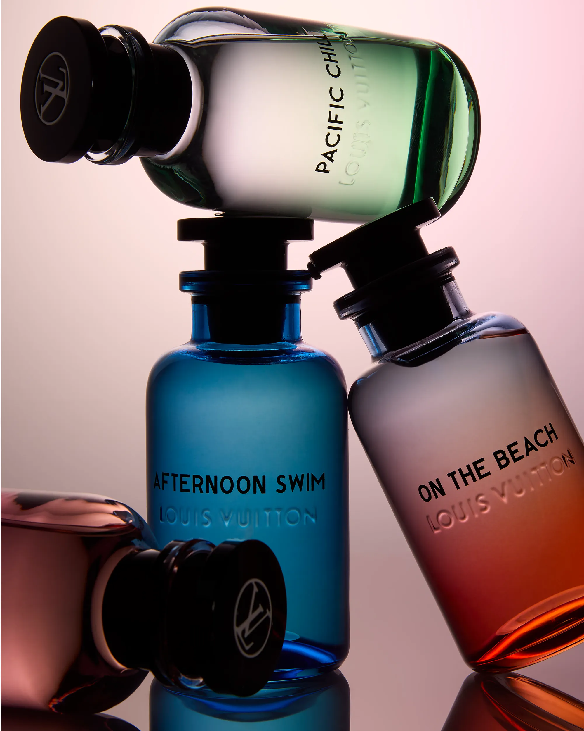 still life photograph of four louis vuitton bottles leaning against each other with one balancing on top. silhouetted against dark gradiated red background 