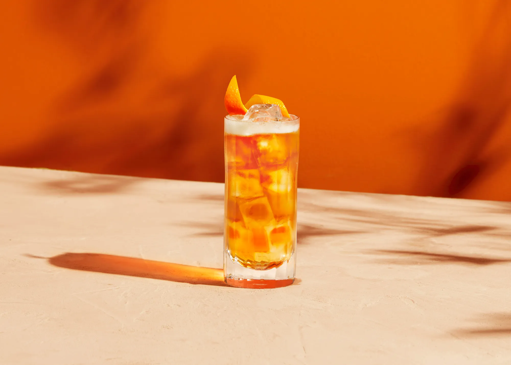 still life photograph of metaxa orange cocktail in evening sun. orange background and reflection of liquid on the surface. faint shadows of branches on the background